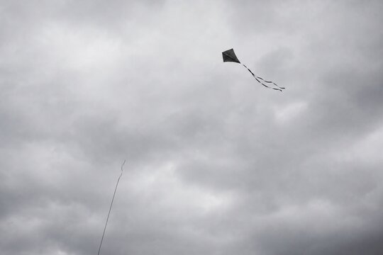 Broken kite string, kite drifting away in gray overcast sky, minimalist composition.