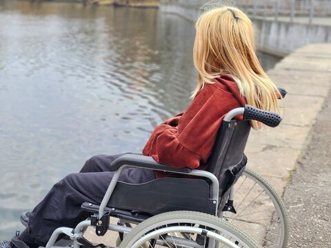 A teenage child is sad and thoughtful in a wheelchair, looking at the water while sitting