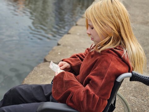 A teenage child in a wheelchair examines pills while sitting