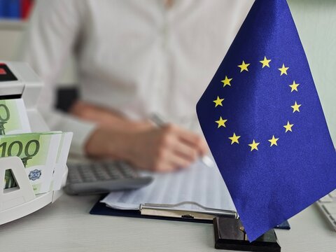 Bank employee records a transaction with European money and displays the European flag
