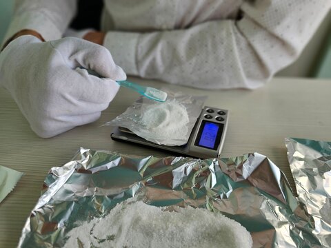 A close-up of a hand pouring cocaine powder or drugs onto foil on a scale