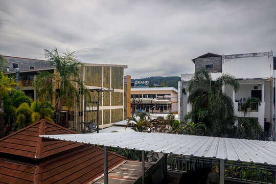 High angle rooftop view of an Asian resort town with buildings and palm trees against a cloudy mountain landscape
