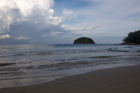 Tropical beach view with incoming waves on the sand and a lush green island coastline under cloudy sky