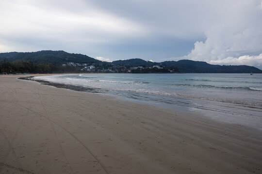 Tropical beach view with incoming waves on the sand and a lush green island coastline under cloudy sky