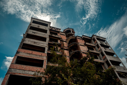 Low angle perspective of a multi story abandoned unfinished brick and concrete hotel structure against a cloudy sky