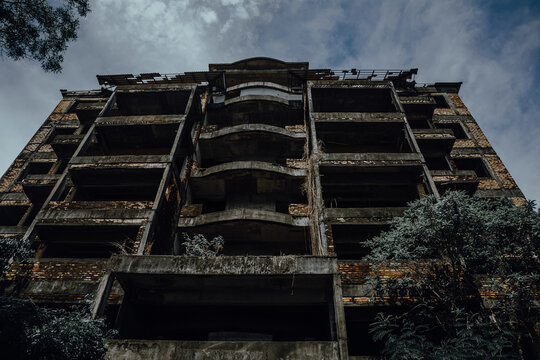 Low angle perspective of a multi story abandoned unfinished brick and concrete hotel structure against a cloudy sky