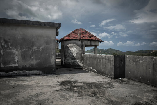 Desolate concrete rooftop of an abandoned resort building with a red tiled alcove under stormy sky
