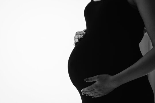 Silhouette of a pregnant woman holding her belly, black and white artistic photo on a white background with empty copy space for text. Concept of motherhood, anticipation, and advertising.