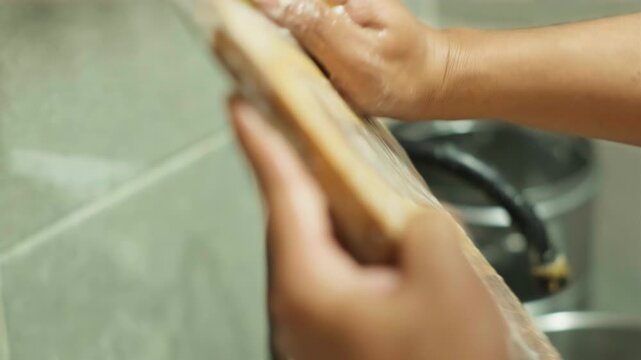 Close up of hands scrubbing wooden cutting board with soap and sponge