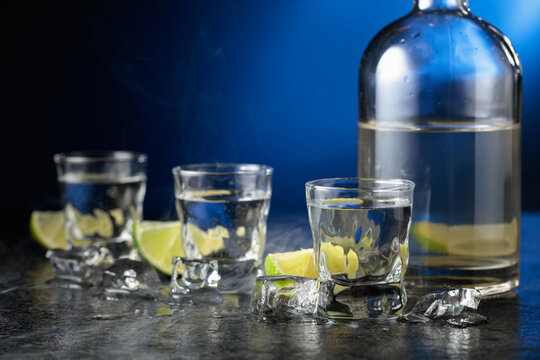 Vodka with lime slices on a black stone table.