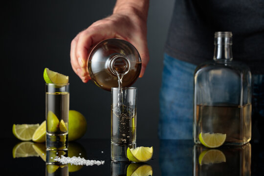 Tequila shots with salt and lime slices on a black reflective background.