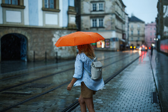 Woman with umbrella crossing street in rush in heavy rain. Extreme weather in summer at city