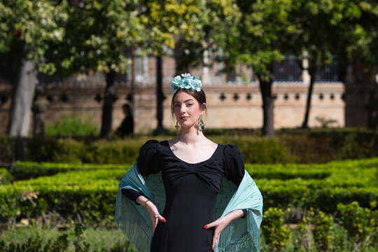 Portrait of a beautiful woman dancing flamenco whilst strolling through a park in Seville. She is wearing a black ruffled dress and a turquoise shawl. Flamenco, a UNESCO Intangible Cultural Heritage.