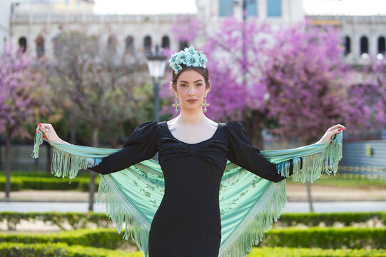 Portrait of a beautiful woman dancing flamenco whilst strolling through a park in Seville. She is wearing a black ruffled dress and a turquoise shawl. Flamenco, a UNESCO Intangible Cultural Heritage.