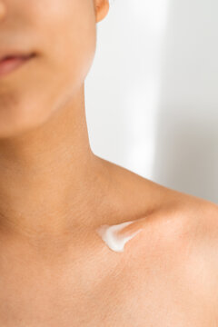 A woman applying moisturizer to her collarbone at home. Skin care