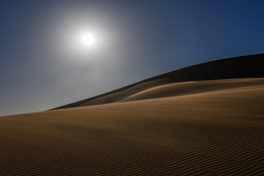 Bright sun shining over sand dunes with wind blowing sand in the desert landscape
