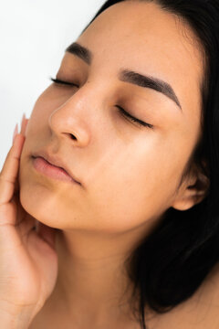 A young woman touching her face with her hand. Natural light, skincare