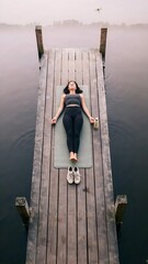 Fototapeta premium Woman Relaxing on Wooden Dock by Calm Water During Morning Light