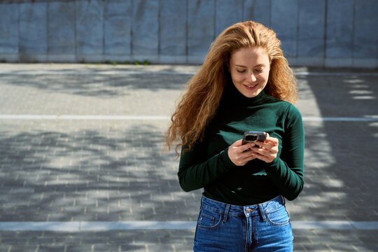 Woman Smiles While Using Smartphone Outdoors on Sunny Day