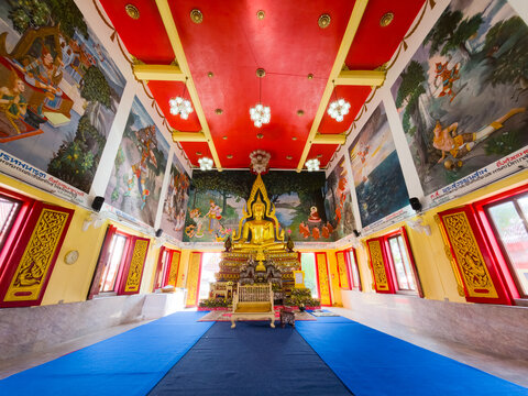 Wide view of a Thai temple interior featuring a golden Buddha statue, red ceiling, and large religious wall murals.