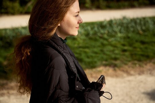 Woman Walking in a Park Holding a Device on a Sunny Day