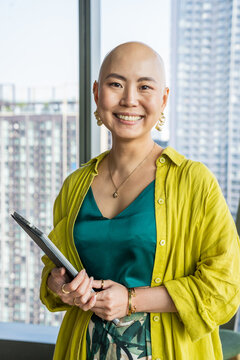 Professional Asian Woman Smiles in Office With City View Behind Her