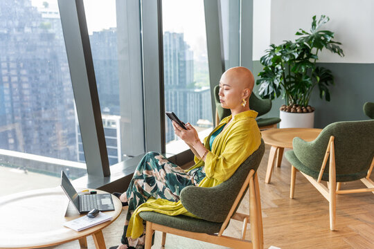 Businesswoman Sitting in Modern Office Space While Using a Smartphone
