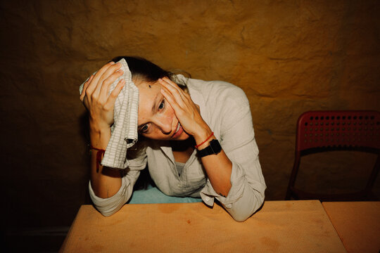 Tired Woman pressing a towel to her forehead at a Table