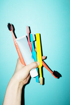 Hand holding toothbrushes and toothpaste in bathroom tile wall
