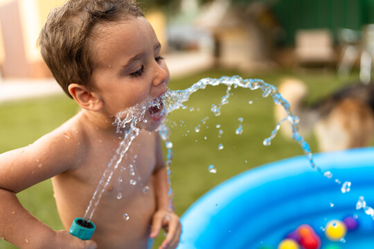 Child drinking water splashing from garden hose