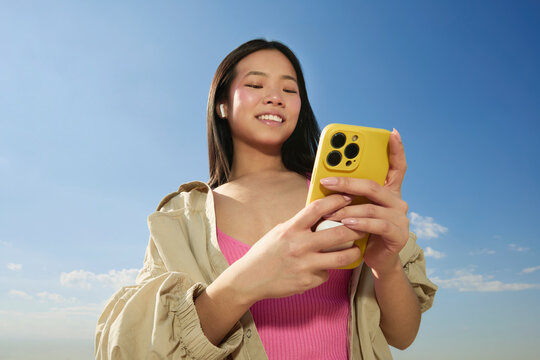 Woman Scrolling Phone Under Blue Sky