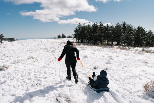 Family pulling child on sled up snowy hill