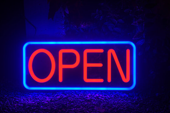 Open neon sign glowing in blue and red light for a retail storefront or business entrance