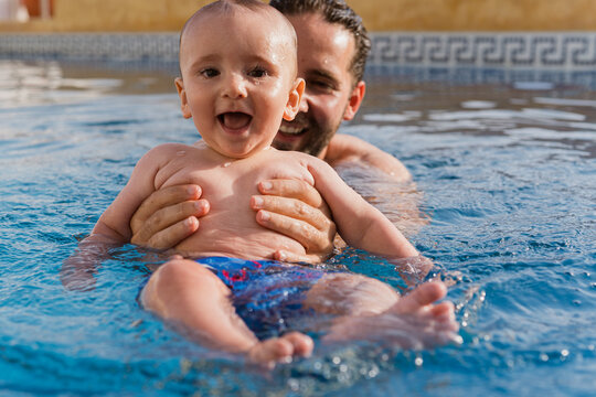 Father holding happy baby in swimming pool