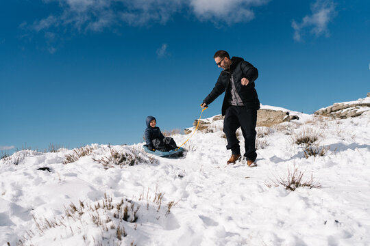 Father pulling child on sled up snowy mountain