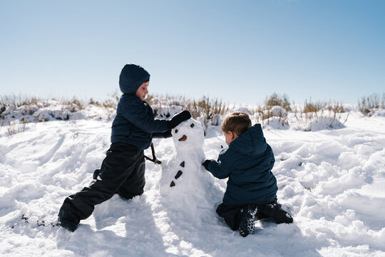 Children building snowman together in deep winter snow