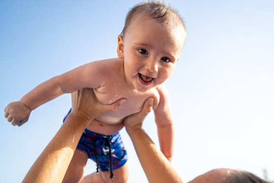 Happy baby playing in water held by parent