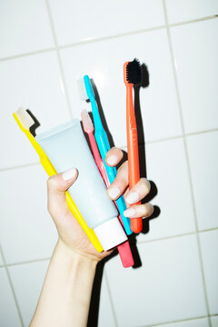Hand holding toothbrushes and toothpaste in bathroom tile wall