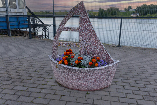 Concrete sailboat flower bed planter with colorful flowers on river embankment