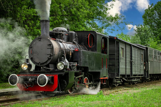 a narrow-gauge steam locomotive in black, belching steam