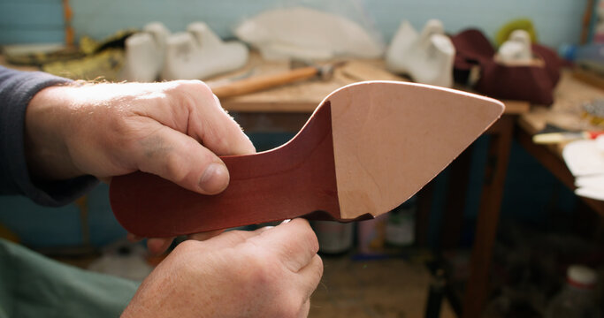 Artisan occupation. Footwear industry. Professional craftsman hands working with leather material shoe sole at workplace.