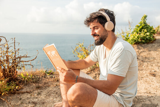 Man enjoying digital detox by ocean cliff reading travel book