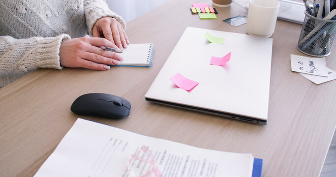 Office workflow. Freelance lifestyle. Unrecognizable female entrepreneur working at desk writing task with sticky notes on laptop indoor.