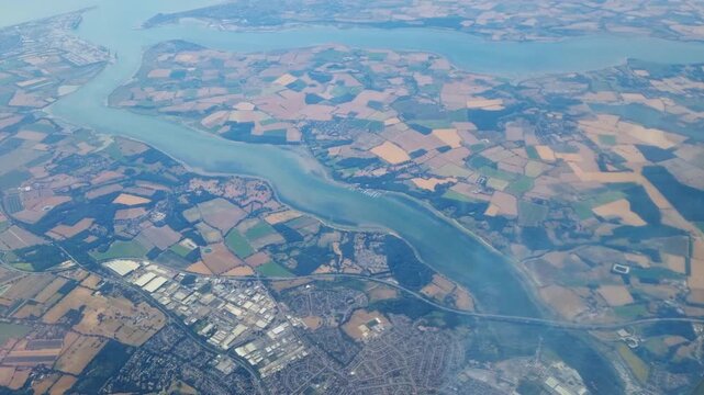 Aerial view of winding river flowing through patchwork farmland and urban areas, showcasing the natural landscape and human development in the region