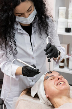Esthetician treatment. Face microcurrent. Woman in black gloves using professional device for lifting skin modern beauty procedure.