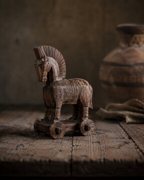Hand-carved wooden Trojan horse figurine on a rustic table, illuminated by soft side light as a symbolic reminder of strategy, deception, and ancient legend.