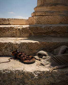 Worn leather sandal and folded woven cloak left on sunlit ancient stone steps, hinting at an unseen traveler from the world of Homeric legend.