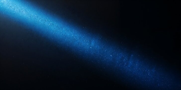 Single bright blue diagonal light beam piercing through dark atmosphere with dust particles floating in air, abstract