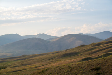 Obraz premium Vast open hills fade into layered mountain ridges under a partly cloudy sky