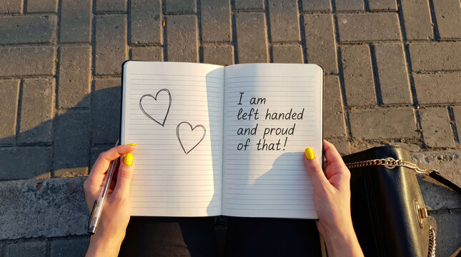 Person holding notebook with left-handed pride message and hearts